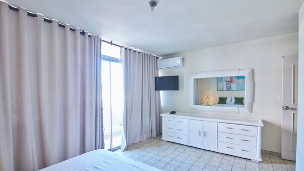 A hotel room with a bed, a TV, a dresser, and a window with curtains.