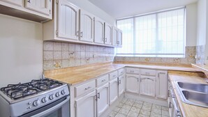 A kitchen with white cabinets, a gas stove, a sink, and a window with blinds.