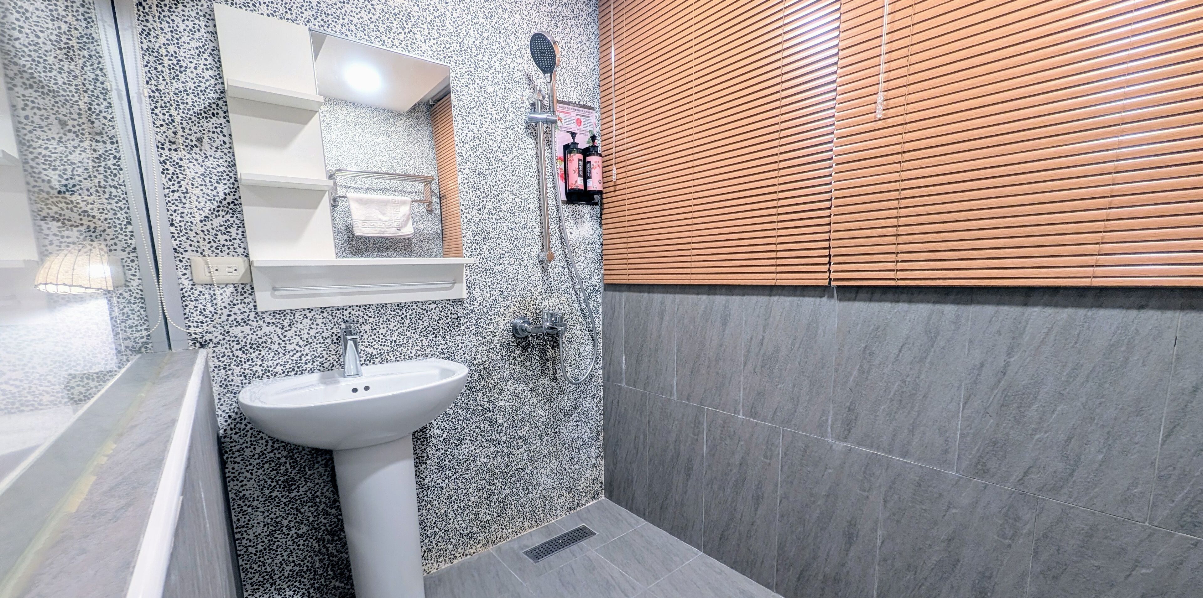 Une salle de bain avec un lavabo blanc, un miroir et une douche avec des stores en bois.