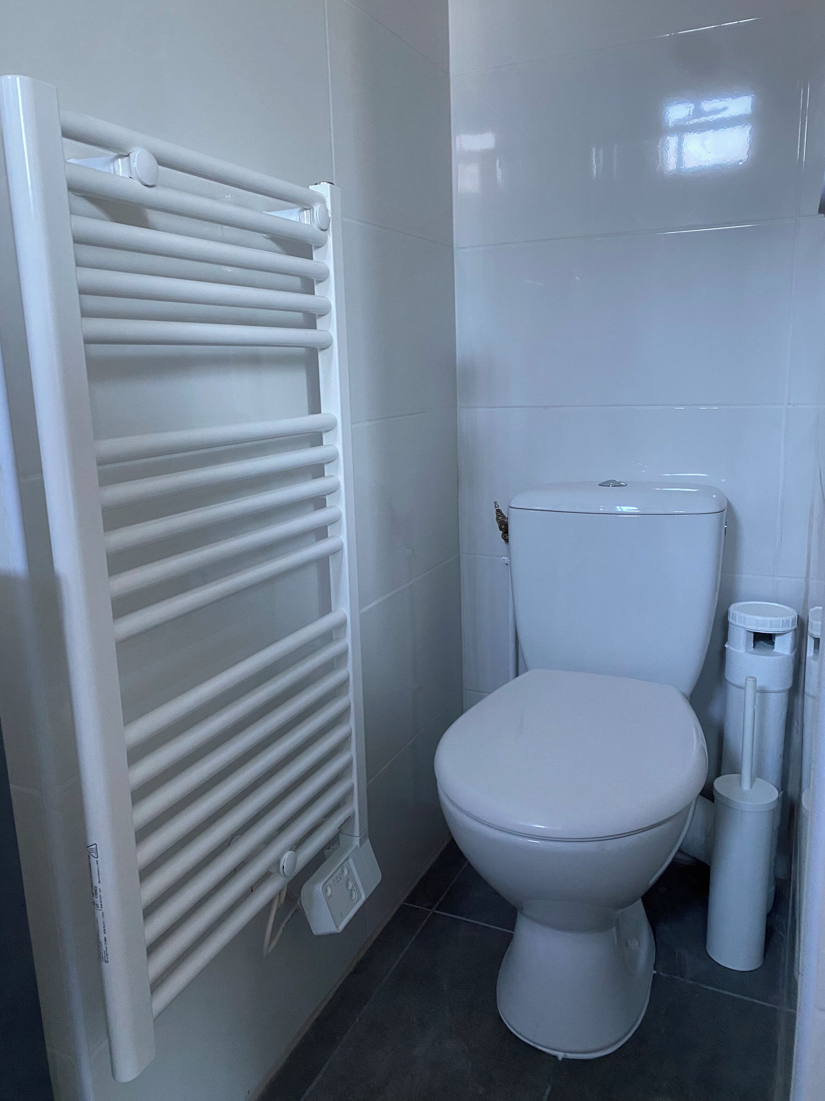 Casa de banho com sanita branca, radiador branco e um contentor de lixo branco.