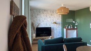 Una sala de estar con televisor de pantalla plana, sofás verdes, una mesa de centro de madera y una lámpara decorativa.