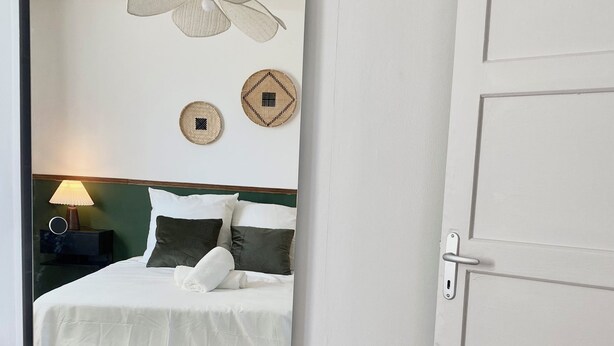 Habitación de hotel con cama, mesita de noche con lámpara, ventilador de techo y decoración en la pared.