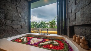 A bathroom with a stone wall, a window, a sink with a heart-shaped flower arrangement, and a chair. - 3Bedroom - 703 - Private Pool Villa Sanur (Denpasar Selatan)