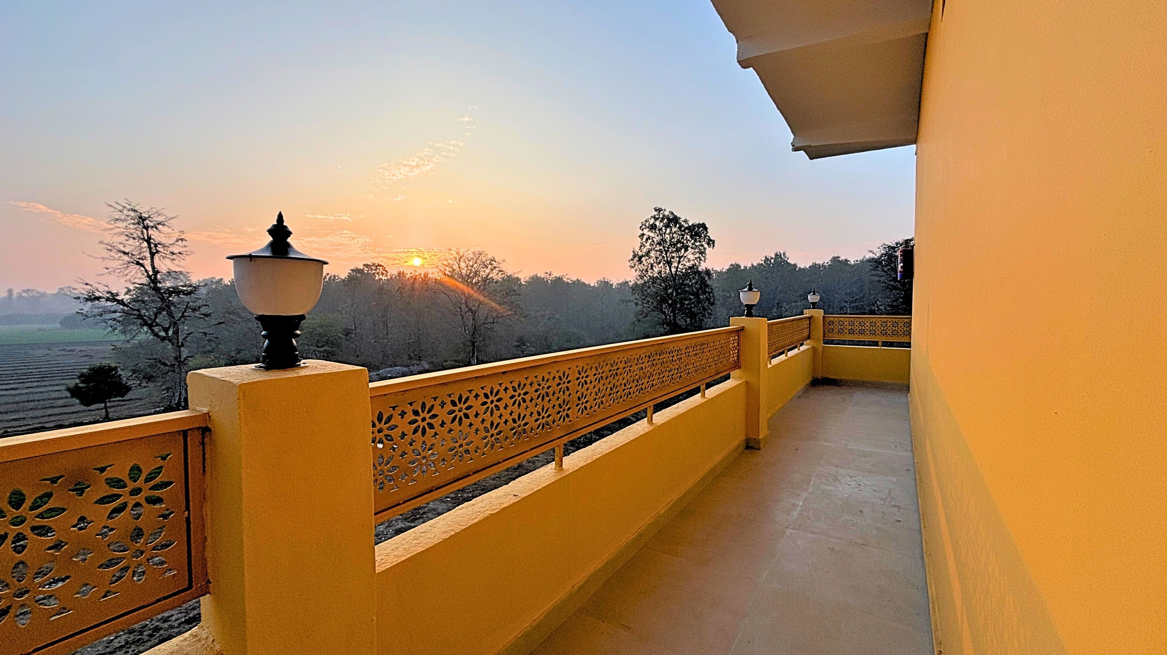 A balcony with a view of a sunset over a forested area.