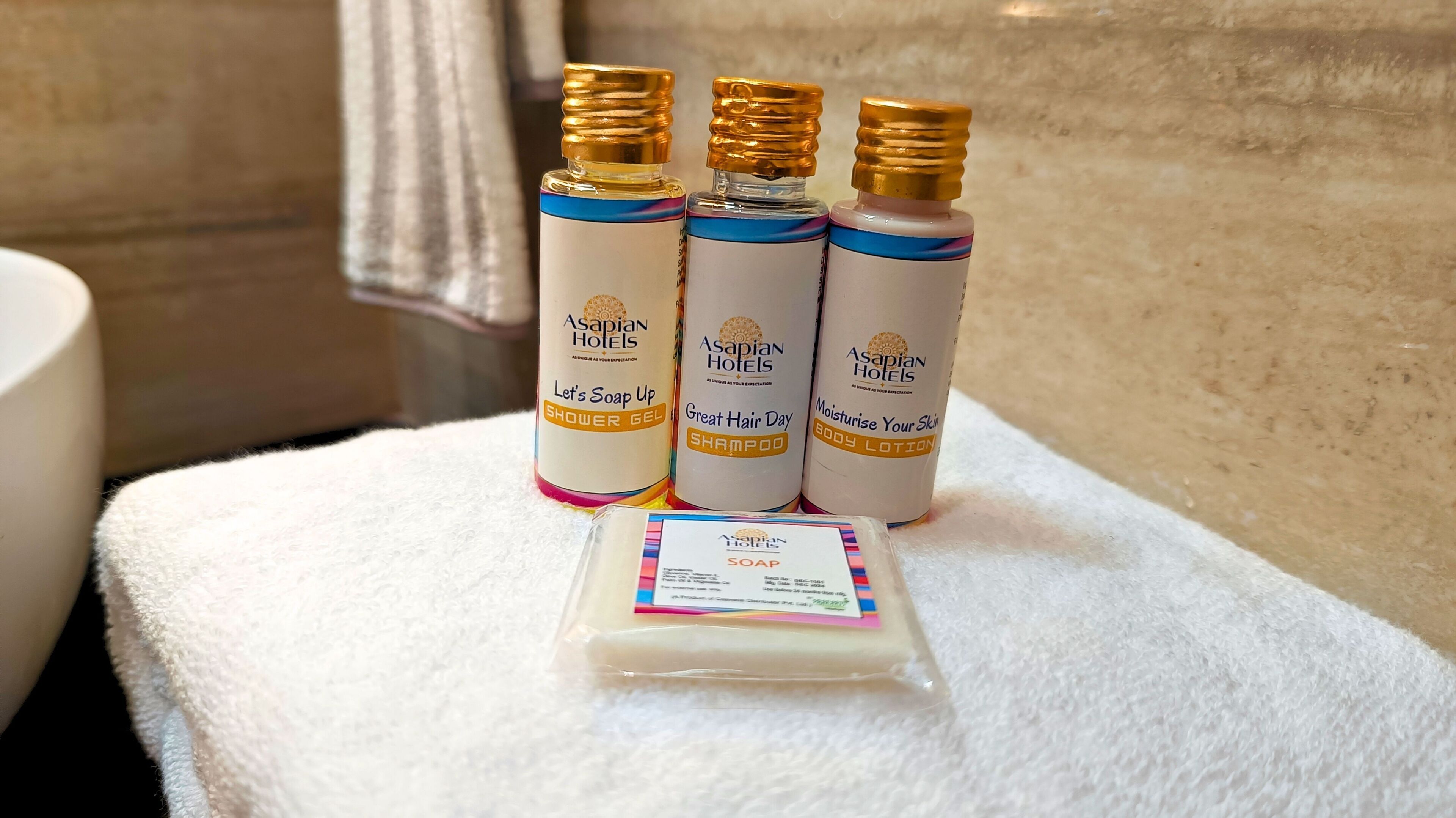 Four bottles of Asapian Hotels products on a white towel in a bathroom.