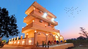 A multi-story building with balconies, a covered outdoor seating area, and a clear sky. - Asapin Vanymahal (Kaladhungi)