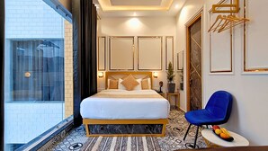 A hotel room with a large bed, a blue chair, a small table with fruit, and a view of the outside. - Asapin Vanymahal (Kaladhungi)