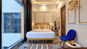 A hotel room with a large bed, a blue chair, a small table with fruit, and a view of the outside.