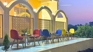 An outdoor seating area with multiple chairs and tables, a decorative fence, and a pool. - Asapin Vanymahal (Kaladhungi)