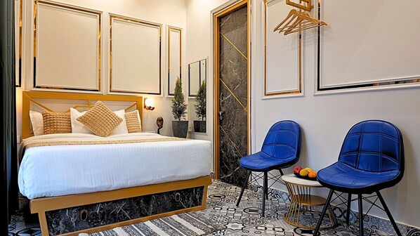 A hotel room with a large bed, two blue chairs, a small table, and a decorative mirror.