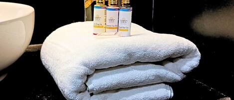 Een stapel witte handdoeken met drie flessen Asapian Hotels producten erboven.