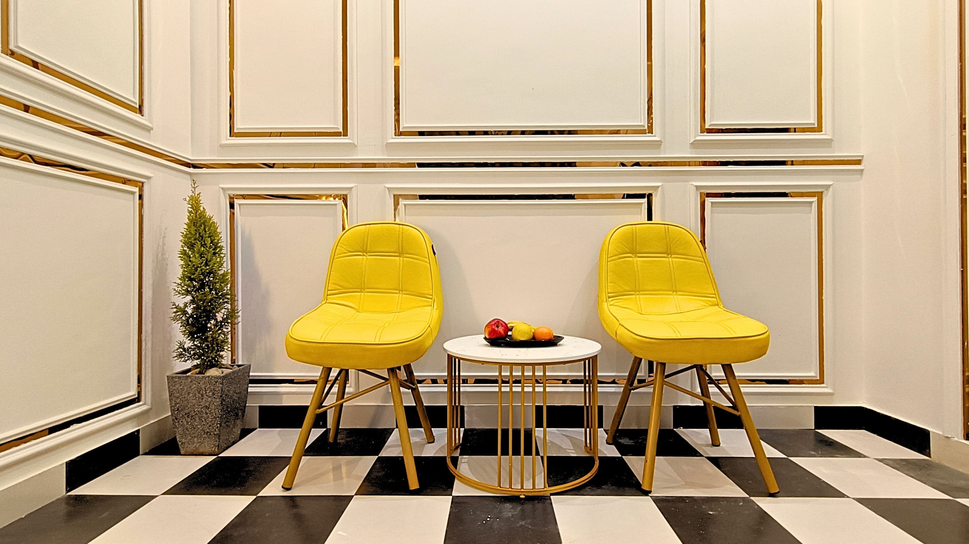 Two yellow chairs with a small round table between them, a potted plant, and a checkered floor.