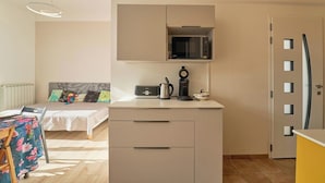 A compact room with a bed, a small kitchenette with a microwave, a coffee maker, and a refrigerator.