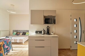 Quarto compacto com uma cama, cozinha compacta com micro-ondas, cafeteira e geladeira.