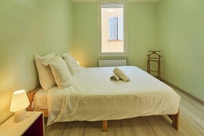 A bedroom with a bed, a nightstand, a lamp, a radiator, and a window with blinds. - Cosy family haven with terrace & light (Toulon)