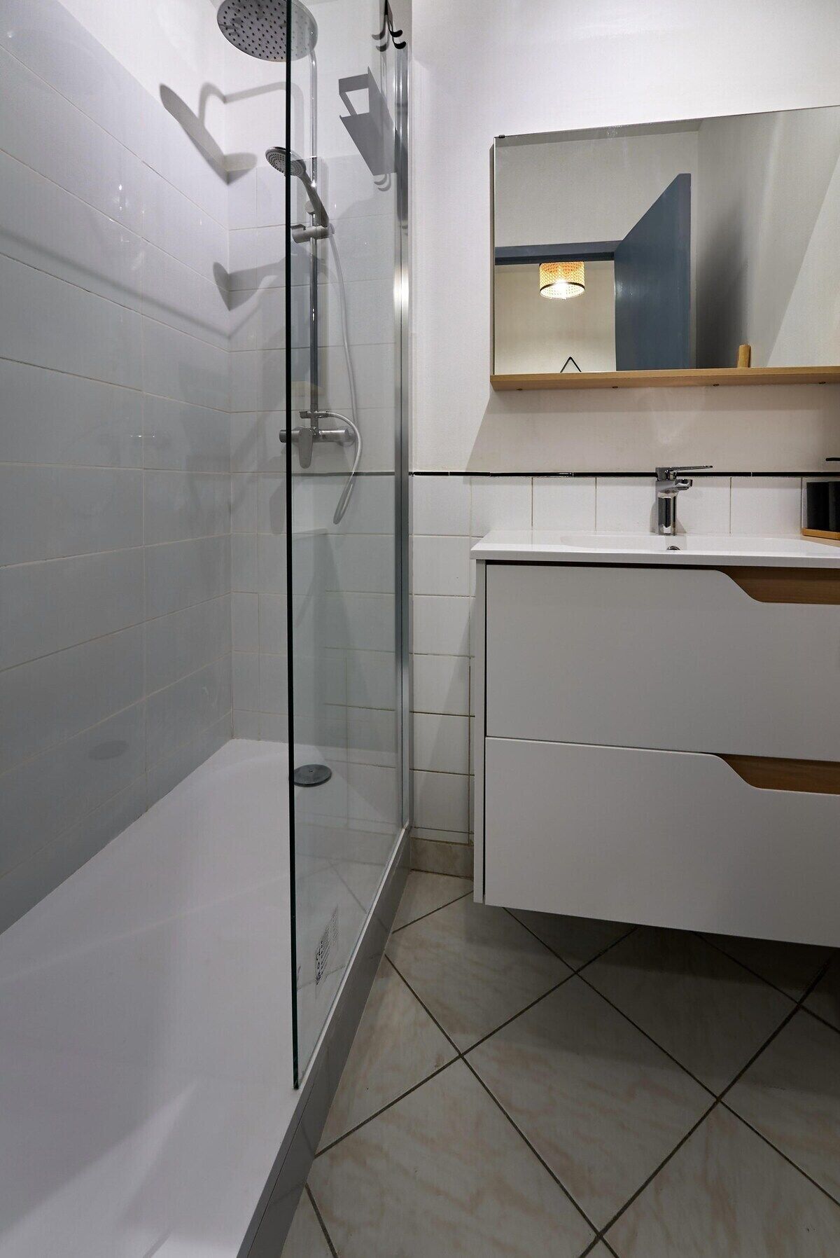 Ein modernes Badezimmer mit einer gläsernen Duschkabine, einem weißen Waschtisch mit Spiegel und Fliesenboden.