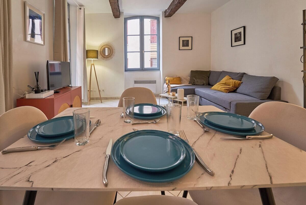 Un coin repas avec une table dressée pour quatre personnes, un canapé et une fenêtre donnant sur un beau paysage.