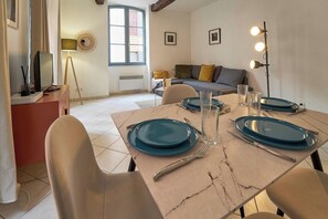 Un coin repas avec une table dressée pour quatre personnes, un canapé, une lampe et un téléviseur en arrière-plan.