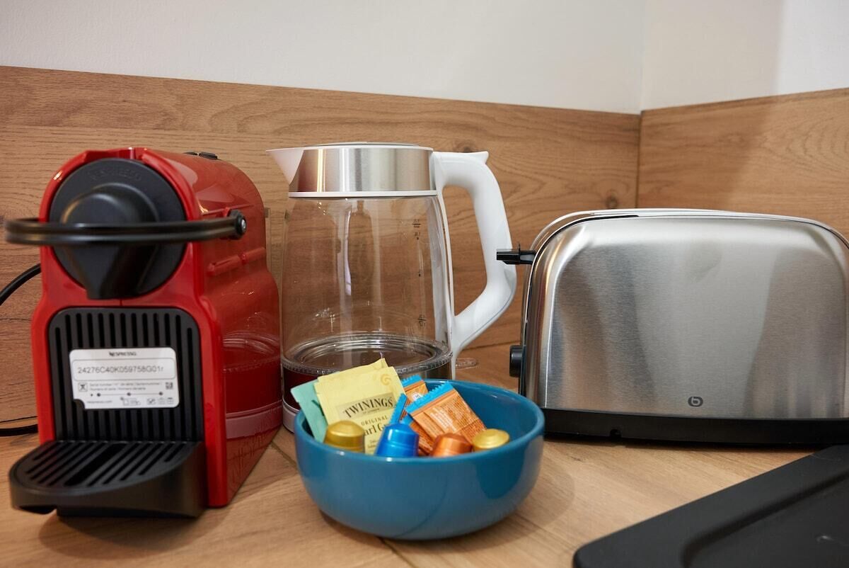 A kitchen with a red coffee maker, a clear glass pitcher, a white kettle, and a silver toaster.