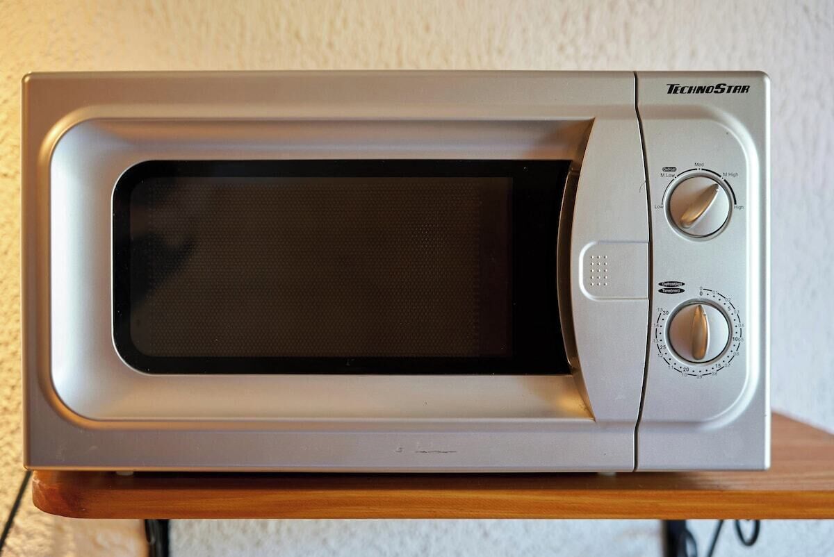 Un four à micro-ondes argenté, doté de deux boutons de commande et d’un écran numérique, posé sur une surface en bois.