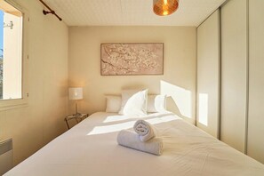 Un lit bien fait, avec une serviette enroulée, une lampe de chevet et une œuvre d’art accrochée au mur.