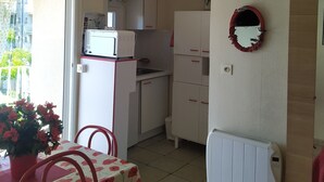 Una cocina compacta con armarios blancos, un microondas integrado y un espejo con marco rojo.