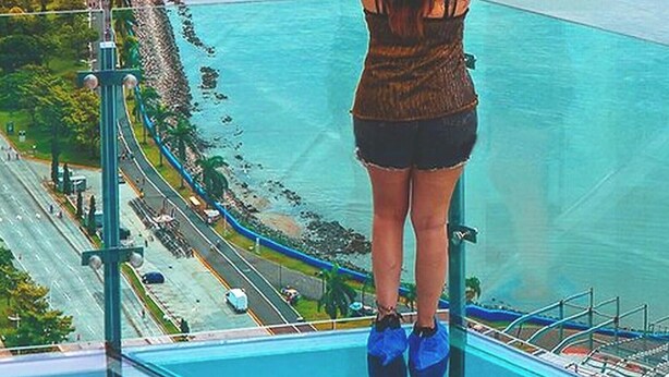 A person standing on a balcony with arms outstretched, overlooking a coastal area with a road and greenery. - 80m² Luxury Ocean View Apartment PH The Sands, Next to Hilton (Panama City)