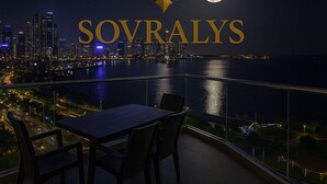 A night view of a cityscape with a table and chairs on a balcony overlooking the water. - 80m² Luxury Ocean View Apartment PH The Sands, Next to Hilton (Panama City)