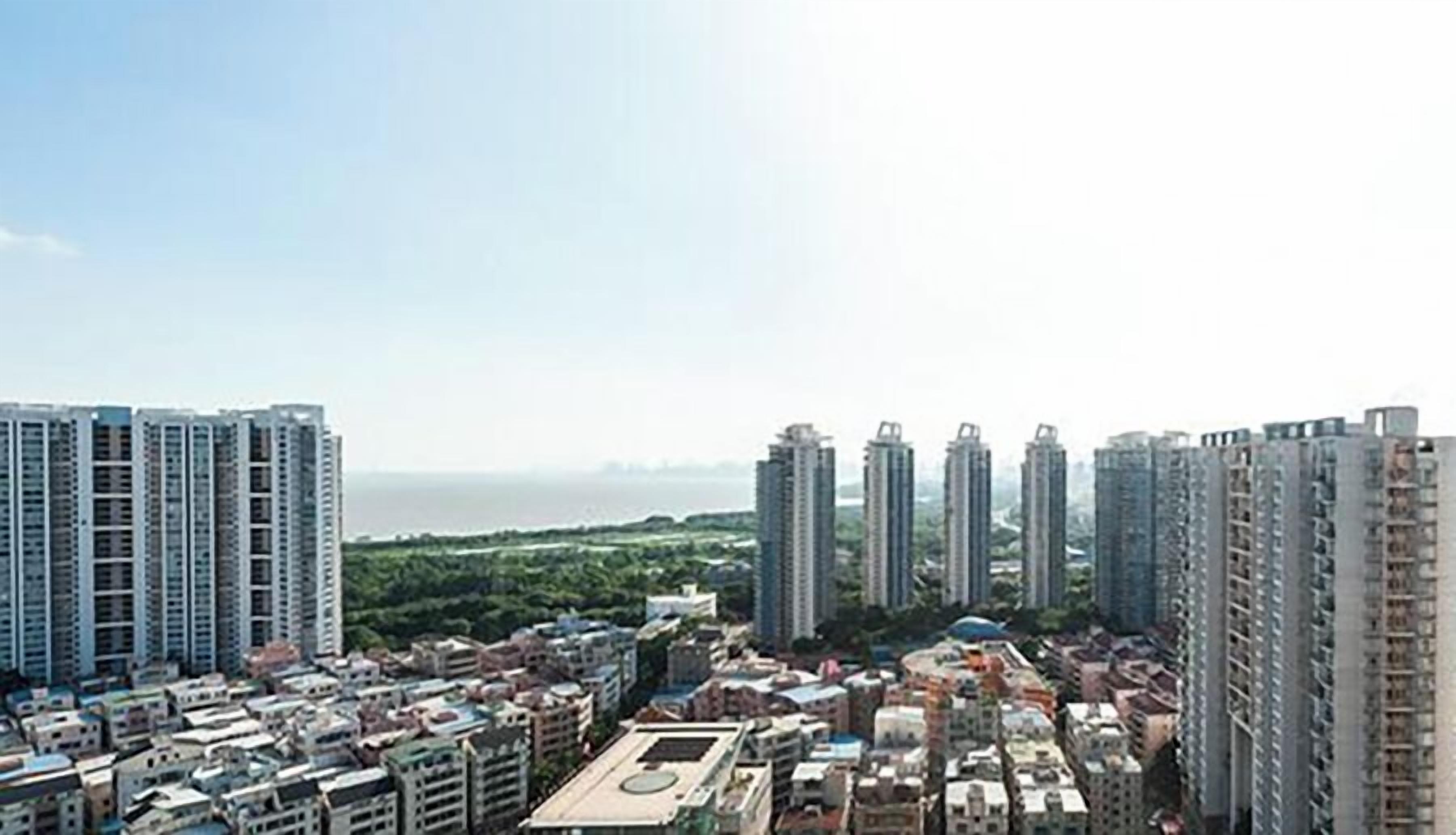 A high-rise residential area with multiple apartment buildings, a central open space, and a distant view of a body of water.