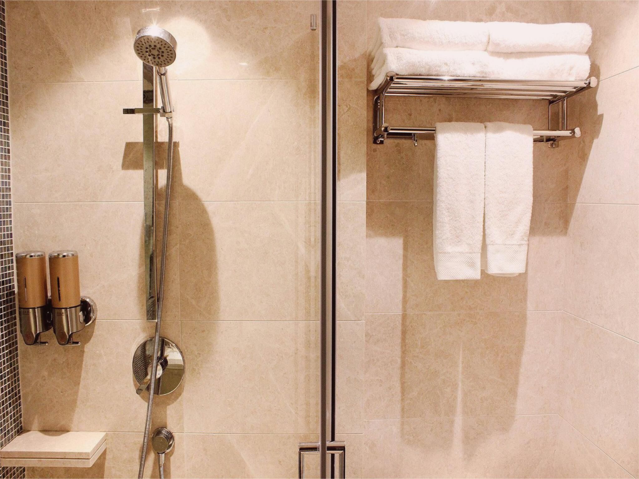 Ein modernes Badezimmer mit einer gläsernen Duschkabine, einem Handtuchhalter mit gefalteten Handtüchern und zwei Seifenspendern.