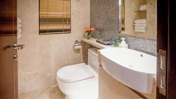 A bathroom with a toilet, sink, and mirror. There is a window with blinds and a towel rack with towels.