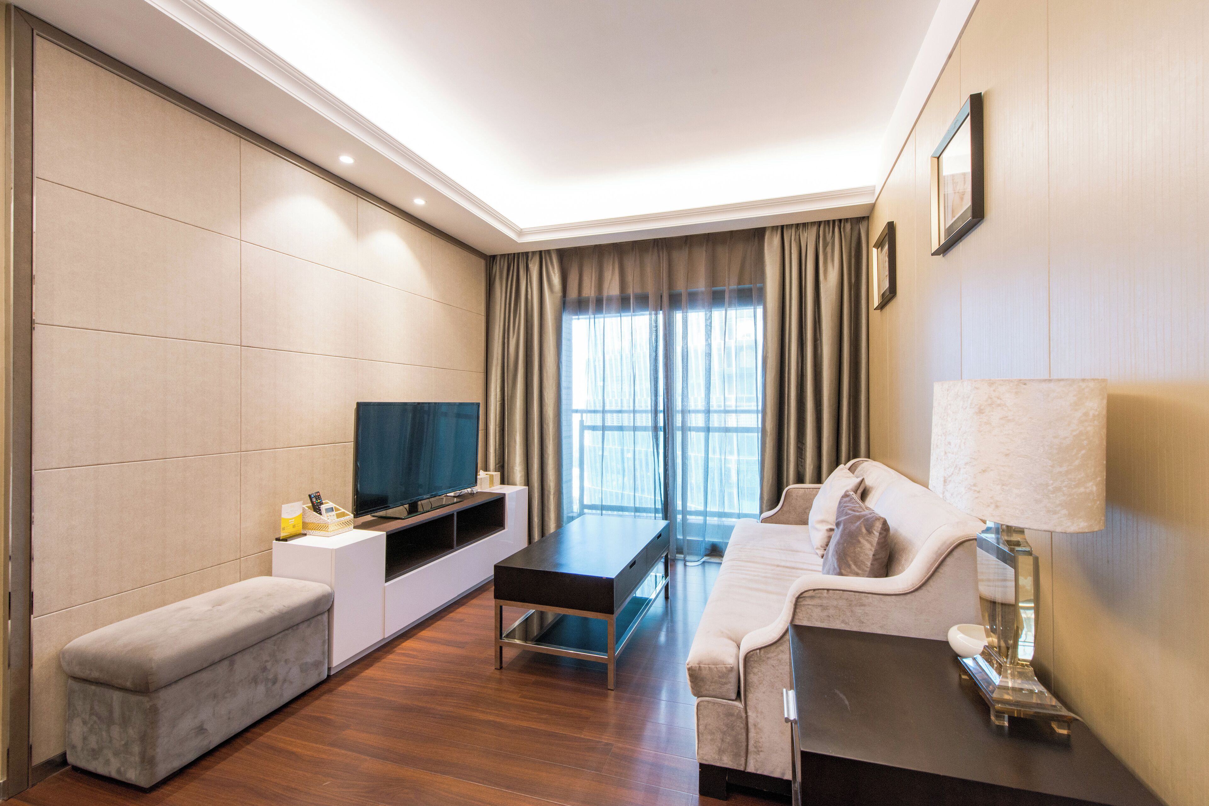 Habitación de hotel moderna con televisor de pantalla plana, sofá, banco y lámpara.