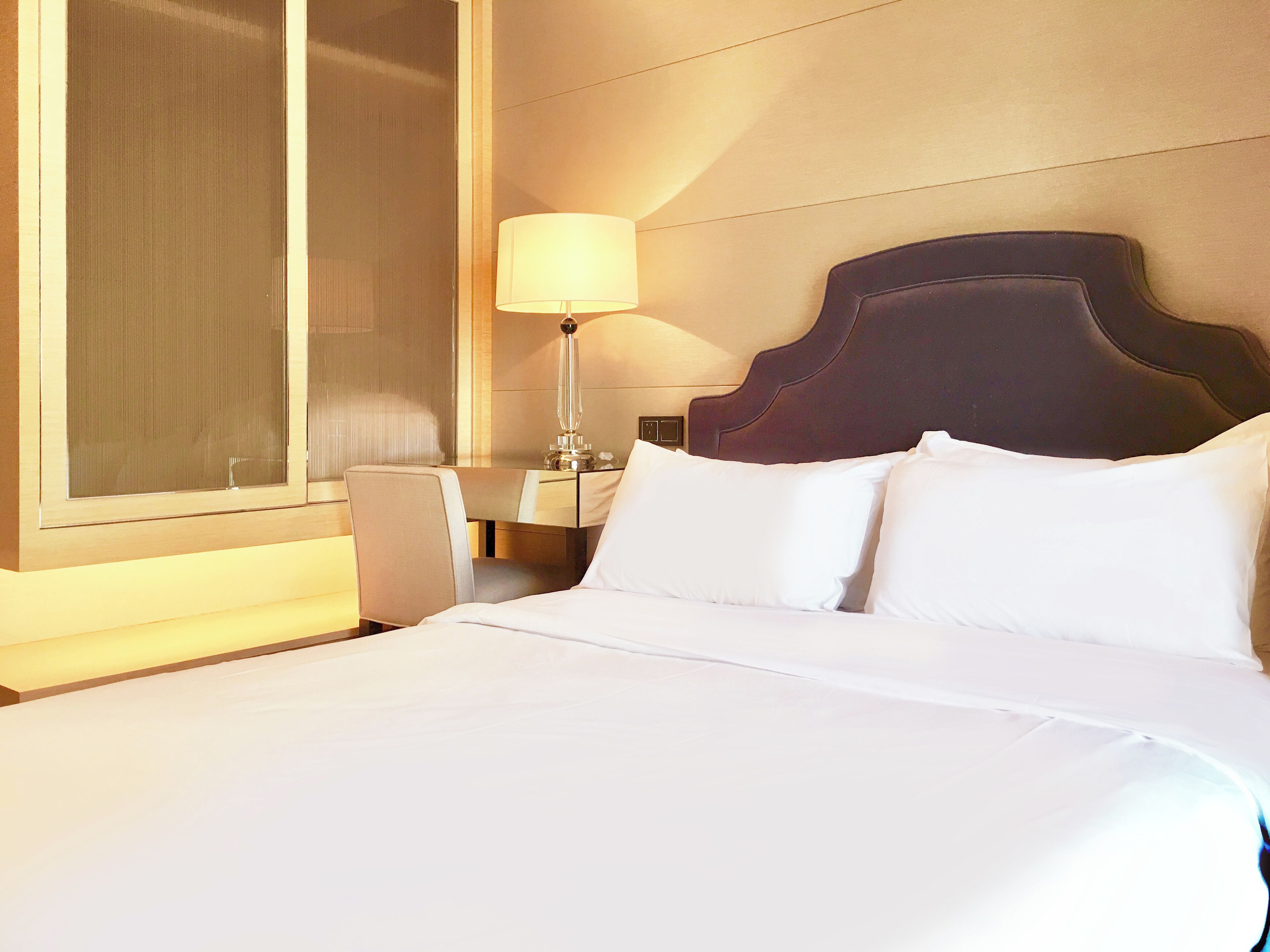 A hotel room with a large bed, a nightstand, a lamp, and a window with blinds.