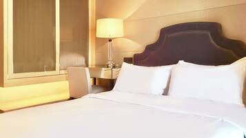 A hotel room with a large bed, a nightstand, a lamp, and a window with blinds.