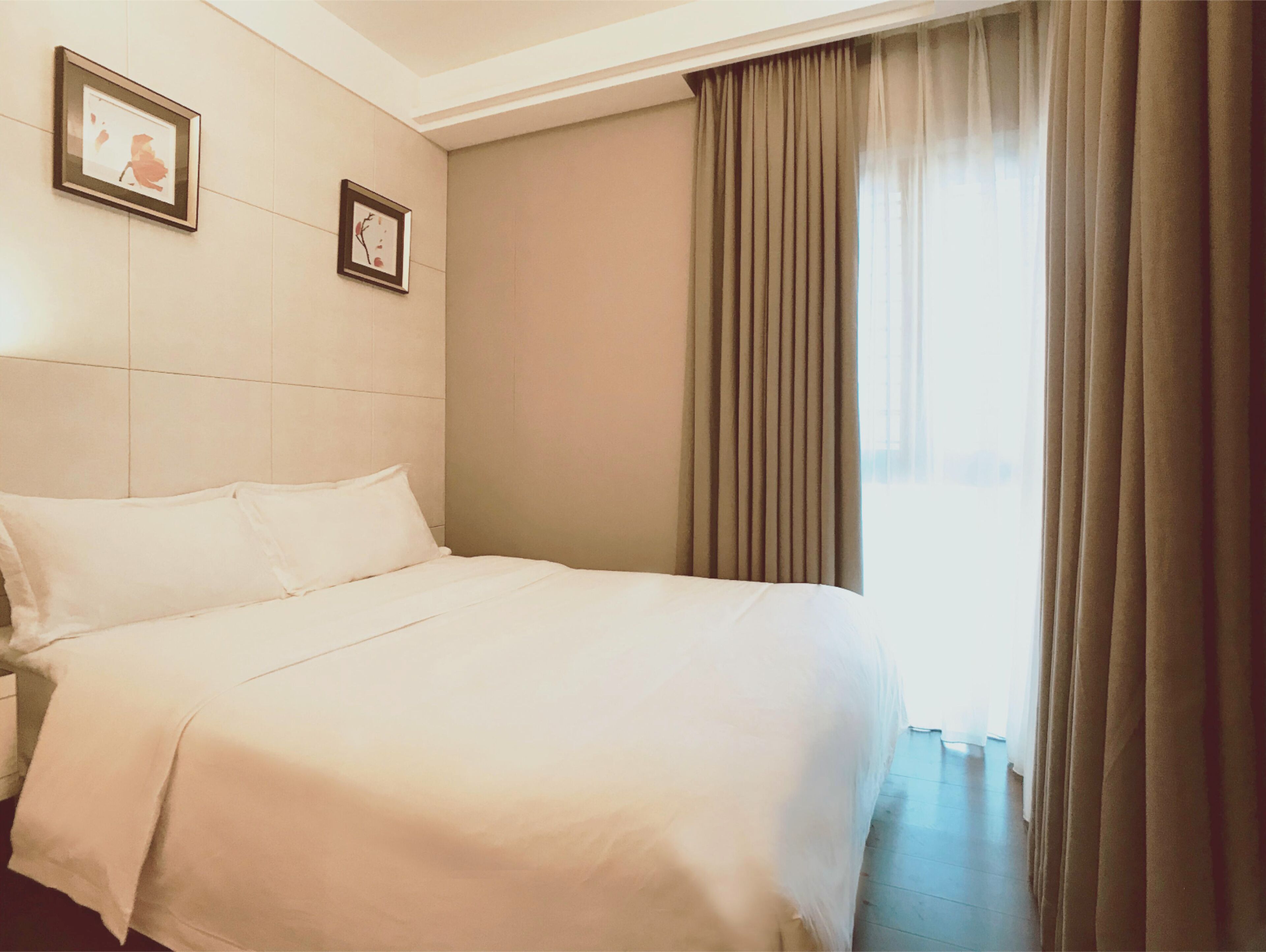 A hotel room with a large bed, two framed pictures on the wall, and a window with curtains.