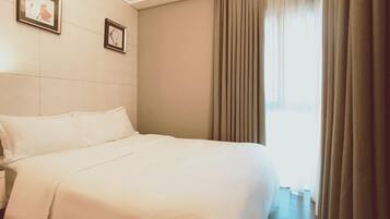 A hotel room with a large bed, two framed pictures on the wall, and a window with curtains.