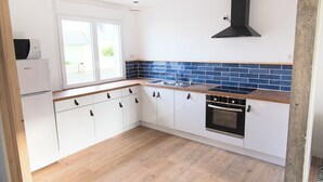A modern kitchen with white cabinets, a black stove, and a blue-tiled backsplash. - Large, bright, quiet house with piano and sunny enclosed garden. (Guilvinec)