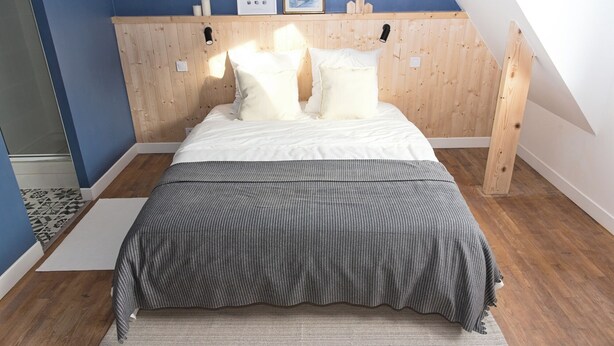 A bedroom with a sloped ceiling, wooden headboard, and a bed with white bedding. - Large, bright, quiet house with piano and sunny enclosed garden. (Guilvinec)