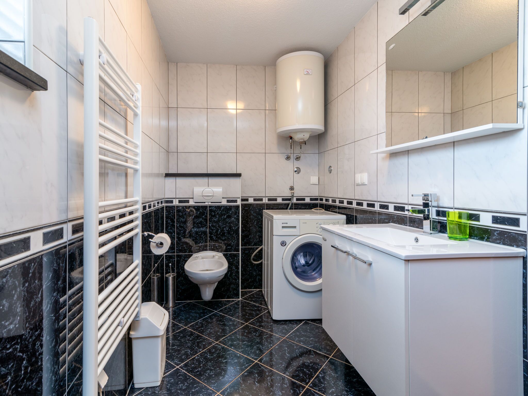 Un baño pequeño con inodoro, lavadora y un perchero para toallas.
