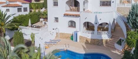 A white villa with a swimming pool, multiple balconies, and a stone facade.