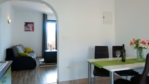 A modern living room with a sofa, a dining table with chairs, and a kitchen area. - Apartment Rosić by Interhome (Krk/Krk)