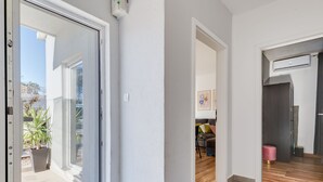 Un intérieur moderne avec une porte-fenêtre coulissante donnant sur un balcon, un couloir avec un plancher en bois et un espace de vie comprenant un canapé et une table basse.