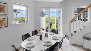A dining area with a round table set for six, chairs, a vase with flowers, and a view of the outdoors through a glass door. - "Casjen" - 250m from the sea by Interhome (Bogense)