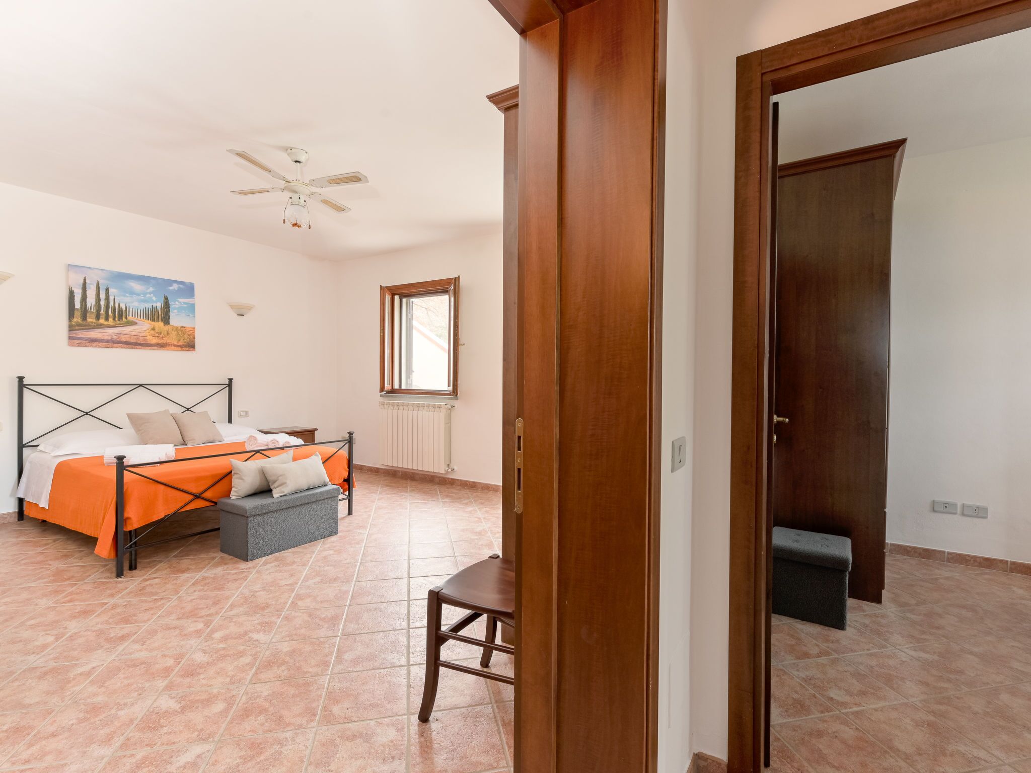 A bedroom with a bed, a chair, a radiator, a window, and a door.