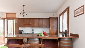A kitchen with wooden cabinets, a granite countertop, a dining table with chairs, and a view of the outdoors. - Il Cipresso by Interhome (Montalcino)