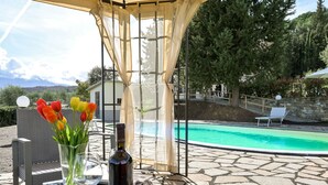 A covered outdoor area with a pool, a table with a bottle and glass, and a vase with tulips. - Il Cipresso by Interhome (Montalcino)