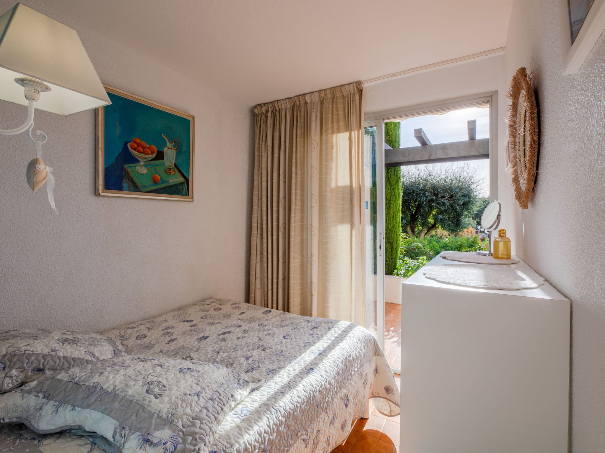 A bedroom with a bed, a painting, a window with curtains, a sink, and a mirror.