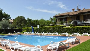 A swimming pool with white lounge chairs arranged around it, a brick pathway, and a building with a tiled roof in the background. - La Casara B by Interhome (Lazise)
