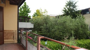A balcony with a metal railing, a tiled floor, and a view of a garden with various plants and trees. - La Casara B by Interhome (Lazise)