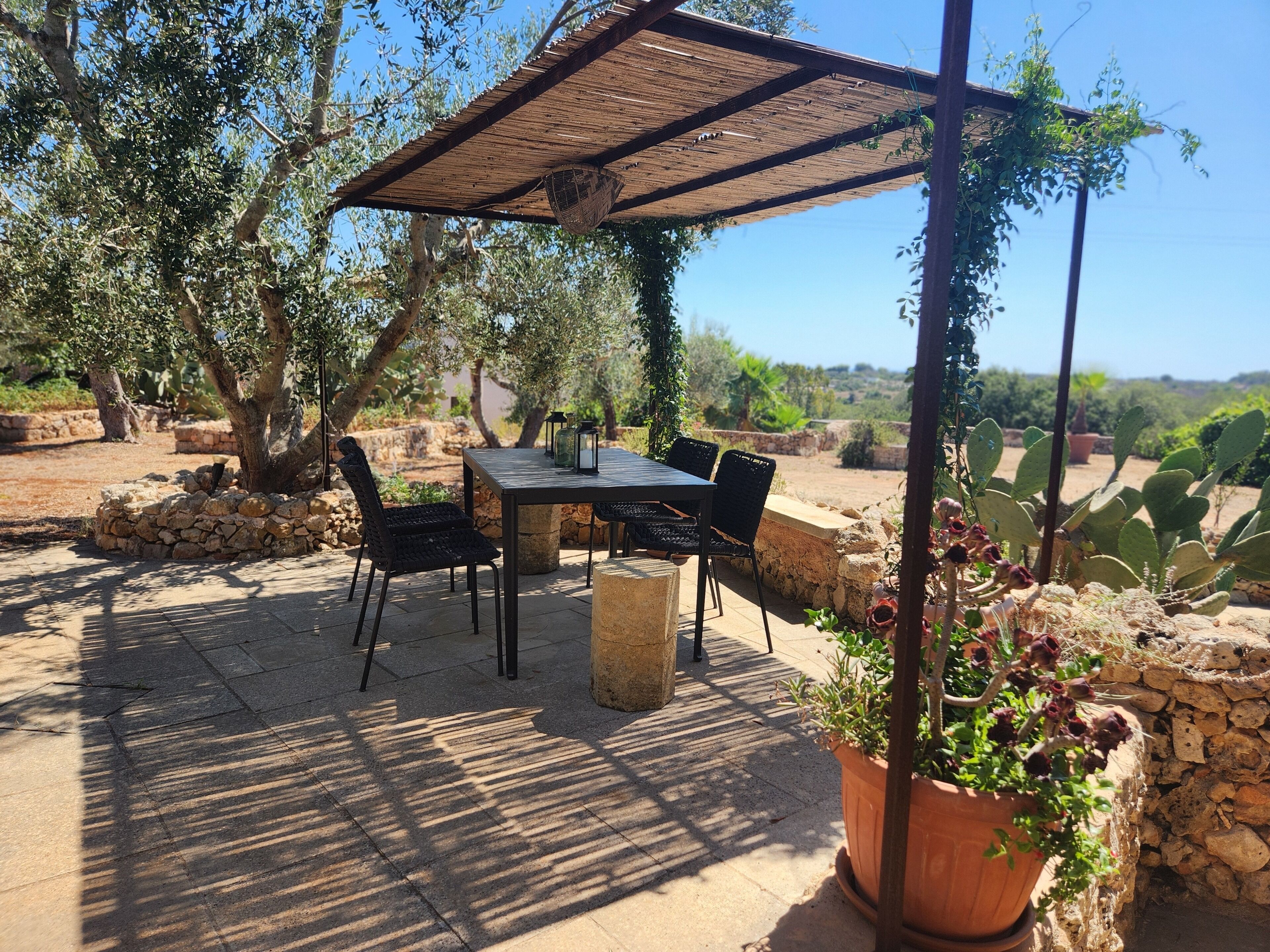 An outdoor patio with a table and chairs, surrounded by stone walls and vegetation.
